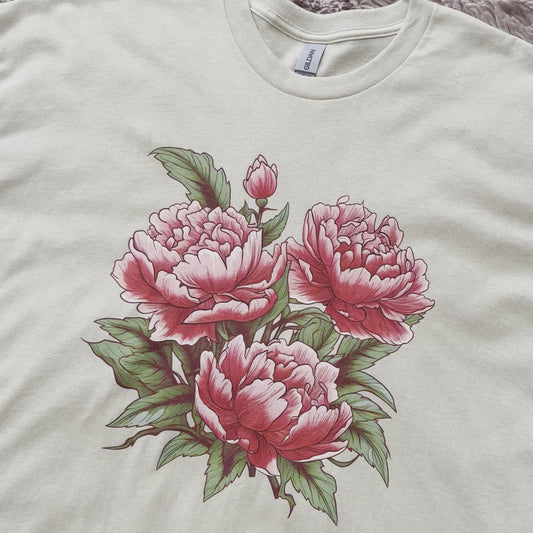 Stylish t-shirt with a drawing of Japanese tattoo art style pink peony flowers. The drawing of the pink peonies stands out against the t-shirt fabric. The drawing of the flowers is intricate and detailed, with a variety of petals and leaves. The colors of the flowers range from light pink to a deep pink. The leaves are dark green in color.